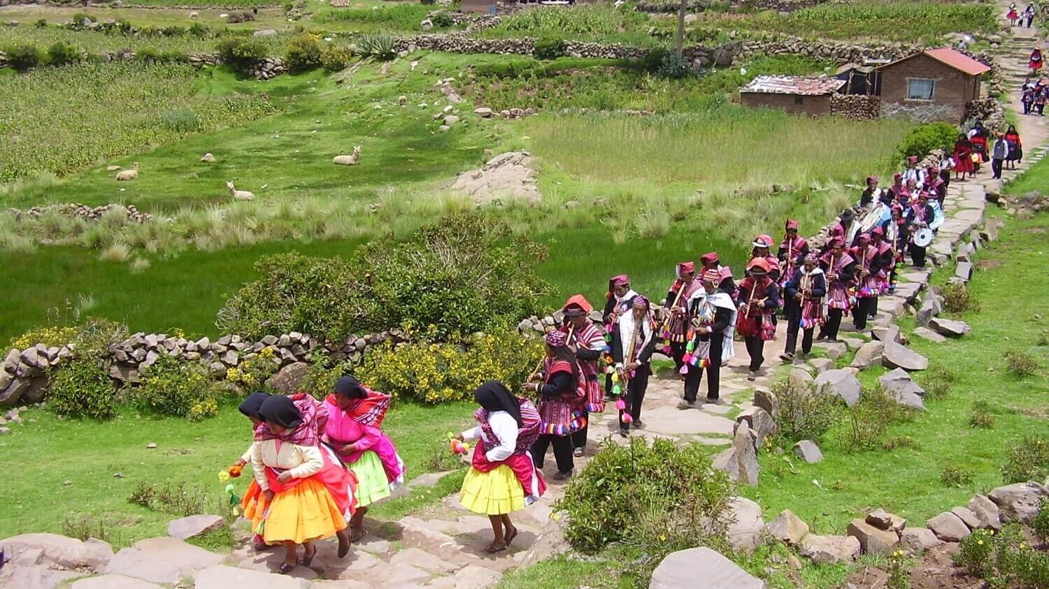 A marching band with dancing women, all wearing traditional dresses for the fiesta, at Taquile island, Lake Titicaca, Peru | RESPONSible Travel Peru