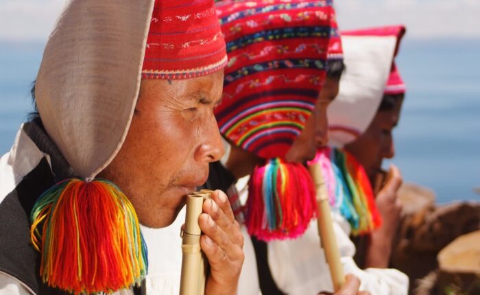Colorful local men from Taquile island playing traditional instruments. Travel deeper with RESPONSible Travel Peru