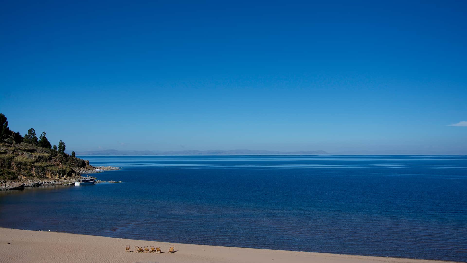 Blue sky and blue water all over, only a small beach line and tiny beach chairs visible | Responsible Travel Peru