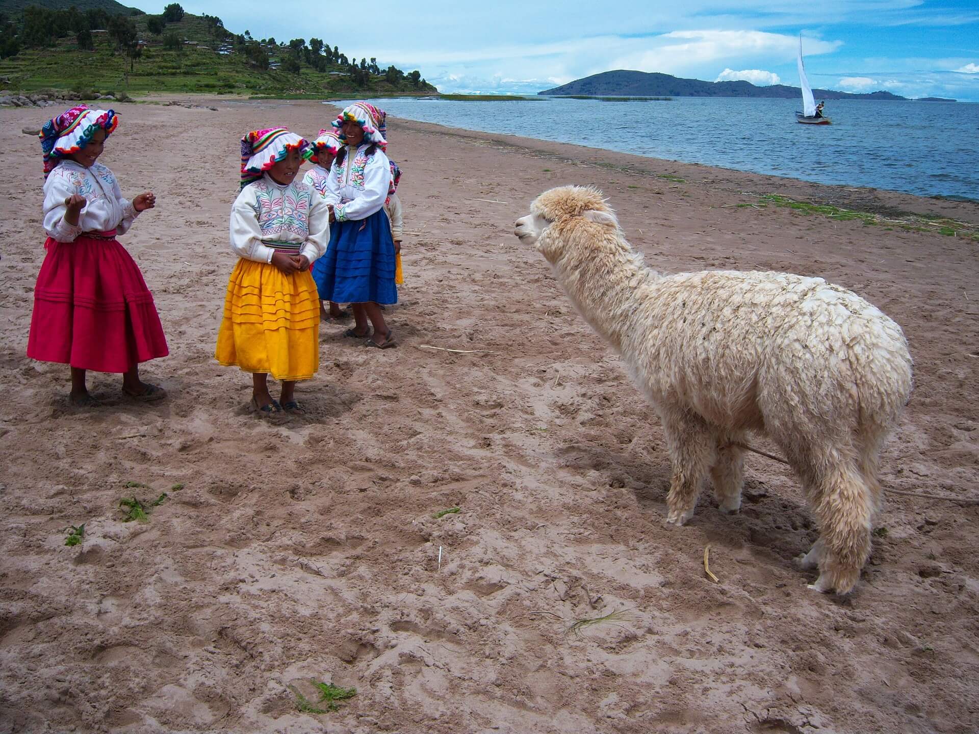 11Traditionally dressed girls from Llachón at the shores of Lake Titicaca with an alpaca and a sailboat. Visit Lake Titicaca in a sustainable fashion and get off the beaten path with RESPONSible Travel Peru.