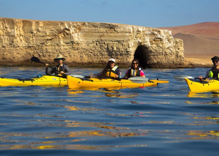 Three bright yellow kayaks over deep blue waters, mountain desert and rock formation in the background | Responsible Travel Peru