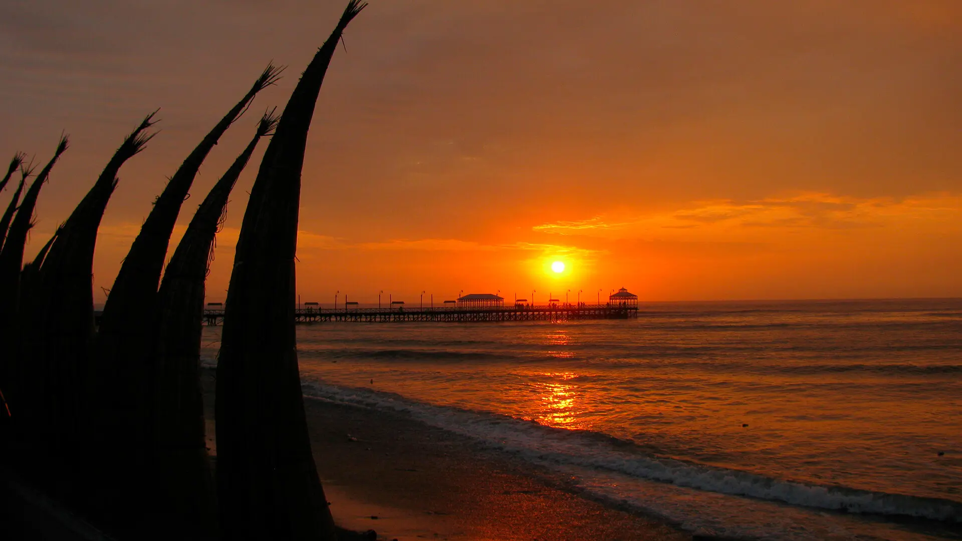 Sunset at Huanchaco beach with a view of its pier and totora boats (caballitos) standing on the shore | RESPONSible Travel Peru