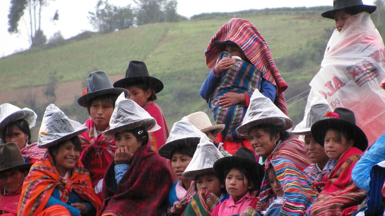 Local women and children protect themselves from the rain by putting a plastic bag on their hats and colorful ponchos around their shoulders.